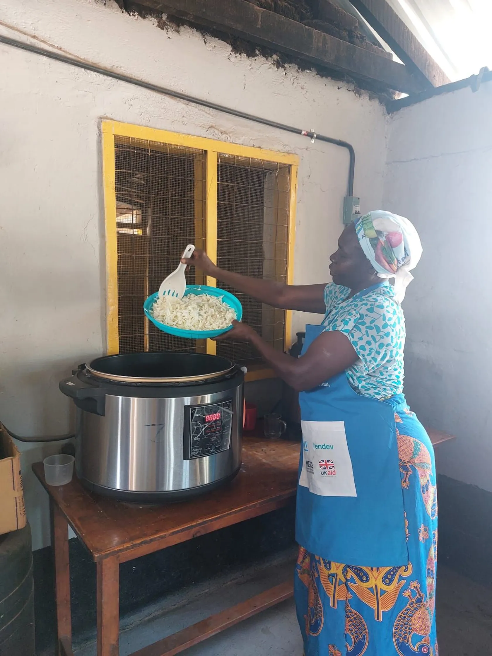 Woman in colorful attire pouring rice into an electric cooker in a kitchen setting