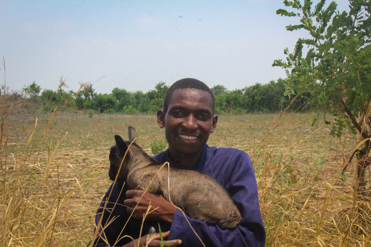 Gift, farmer and pastoralist, poses for a photo with his sheep