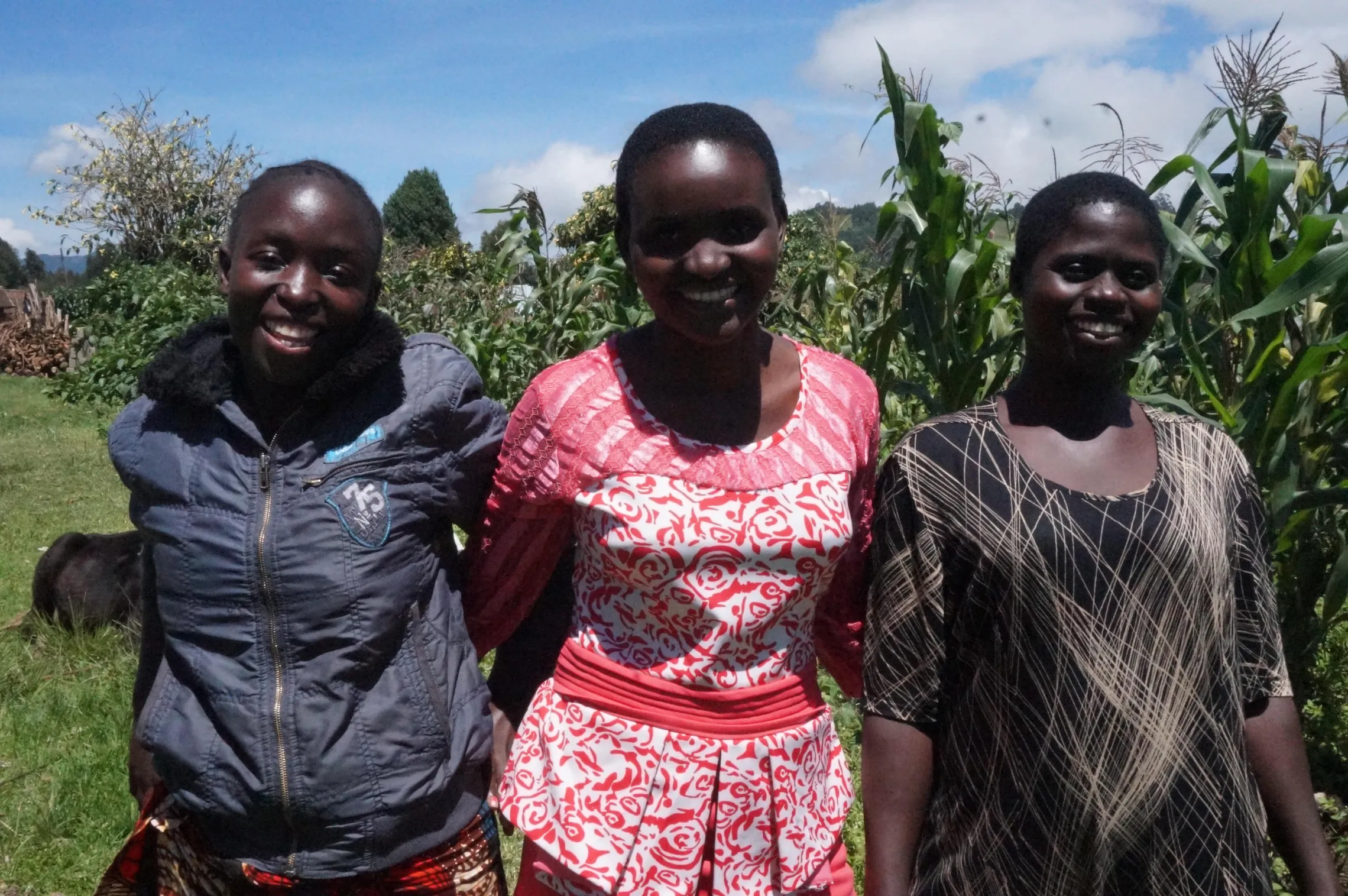 three young women standing together in front of green crops