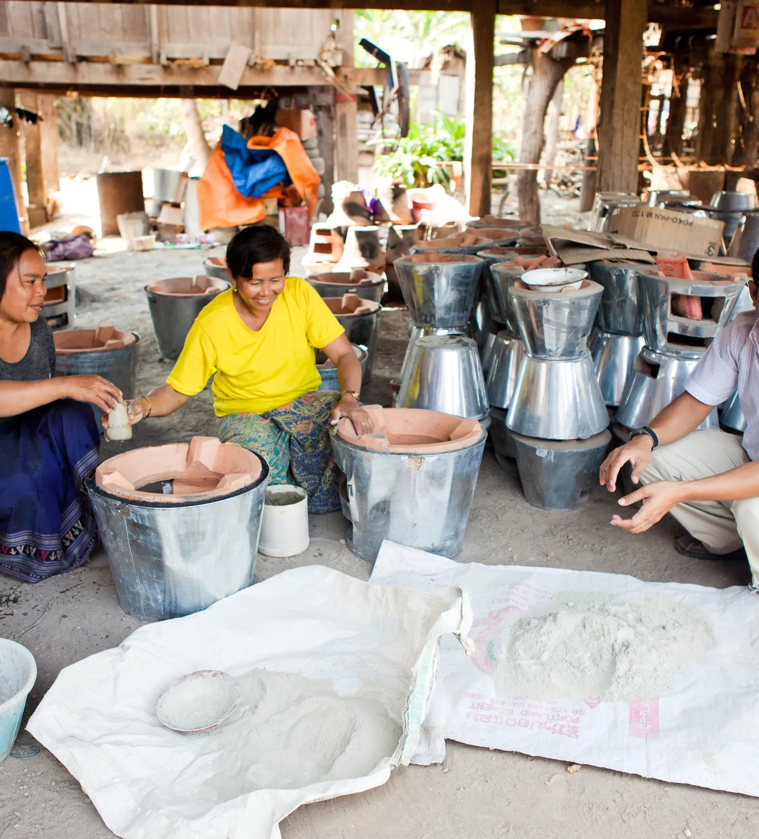 Three people sitting in a rustic workshop, manufacturing improved cookstoves