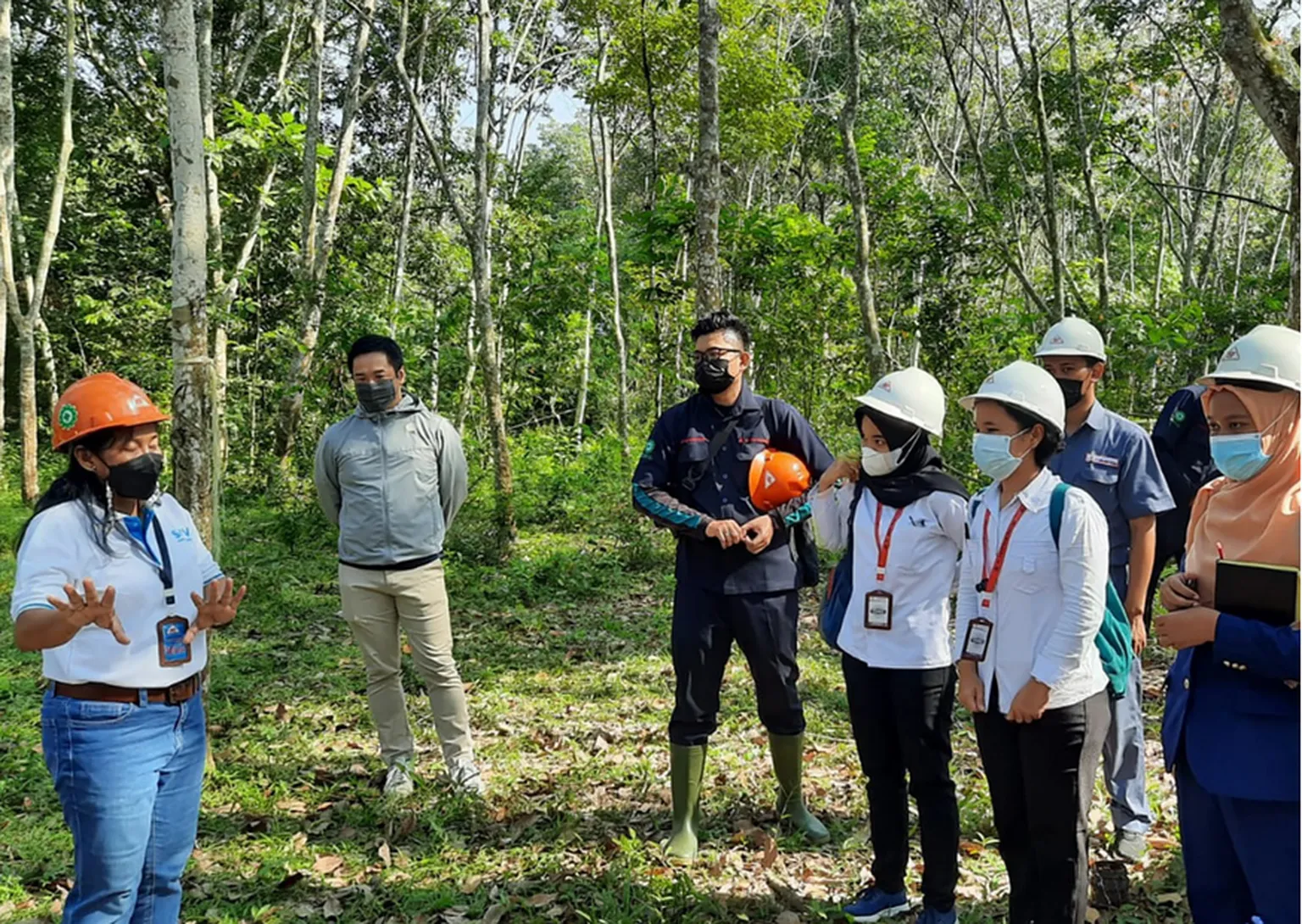 A group of trainees stand in a circle around a trainer in an outdoor forested area